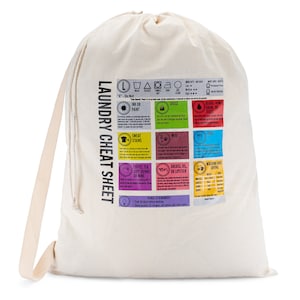 Puede incluir: Una bolsa de lavandería de color crema con cierre de cordón. La bolsa presenta una "Hoja de trucos de lavandería" impresa con consejos para quitar manchas y símbolos de lavandería. El texto incluye instrucciones para quitar tinta, hierba, manchas de sudor y más.
