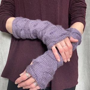 Puede incluir: Un par de calentadores de brazo de punto morado con un patrón de punto de cable.