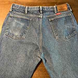 May include: A pair of blue denim jeans with a brown leather patch on the back waistband that says "Premium Quality Wrangler".