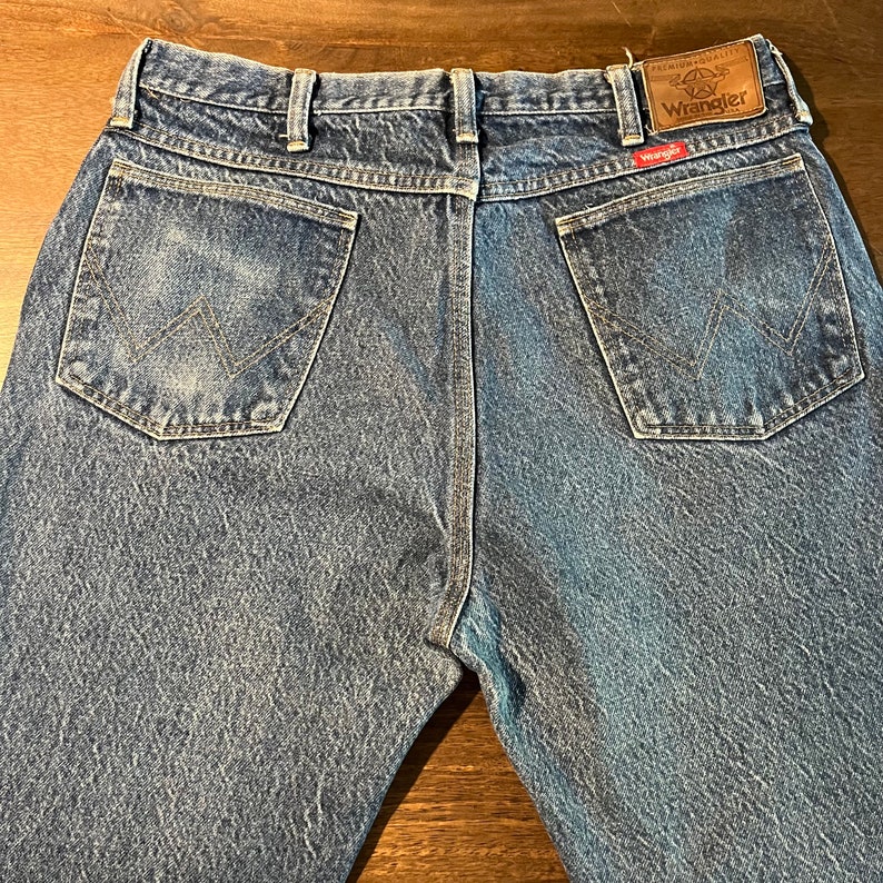 May include: A pair of blue denim jeans with a brown leather patch on the back waistband that says "Premium Quality Wrangler".