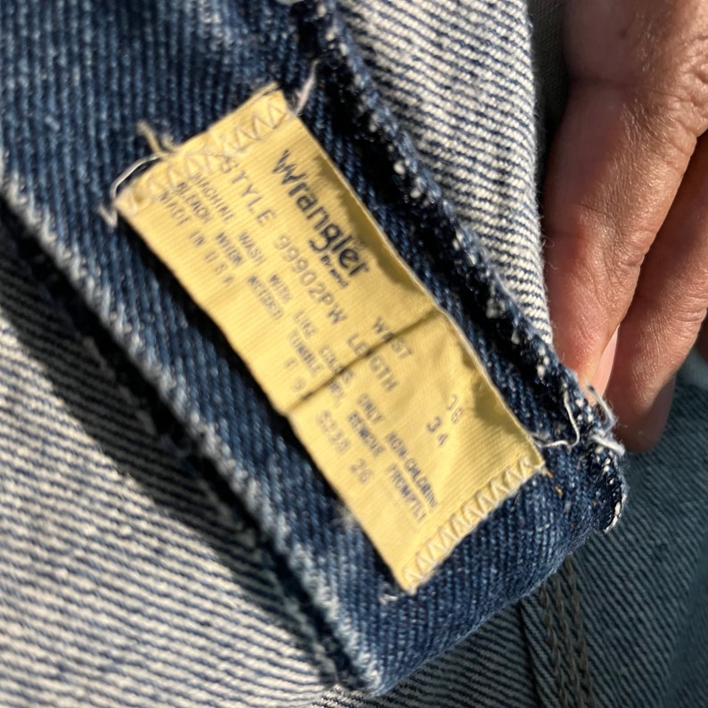 May include: A yellow Wrangler jeans tag with the text "Wrangler", "Style 99902PW", "Waist 36", "Length 34", "Machine Wash With Like Colors", "Only Non-Chlorine Bleach When Needed", "Tumble Dry Low", "Remove Promptly", "Made in USA", "95235 20".