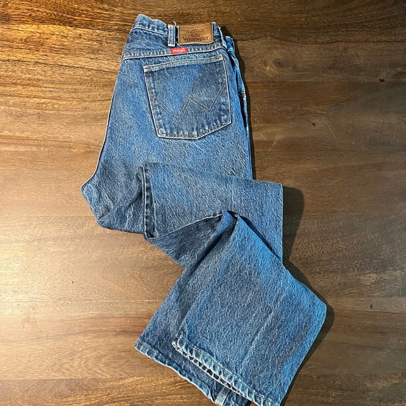 May include: A pair of blue denim jeans with a brown leather patch that says "Wrangler" on the back pocket.