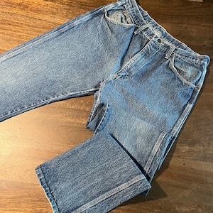 May include: A pair of blue denim jeans with a faded wash and a straight leg fit. The jeans have a classic five-pocket design and a button fly.