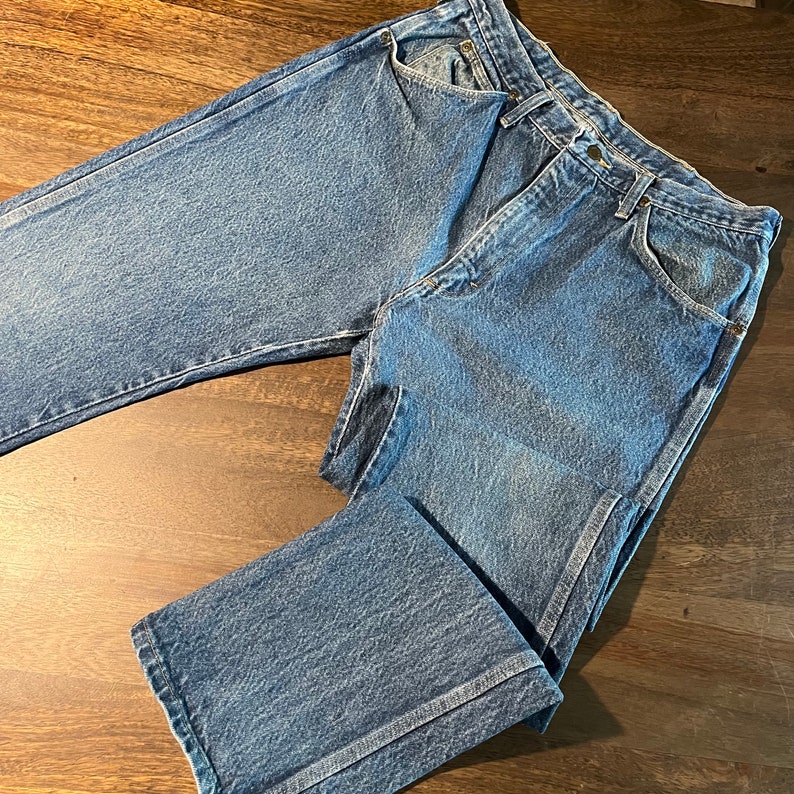 May include: A pair of blue denim jeans with a faded wash and a straight leg fit. The jeans have a classic five-pocket design and a button fly.