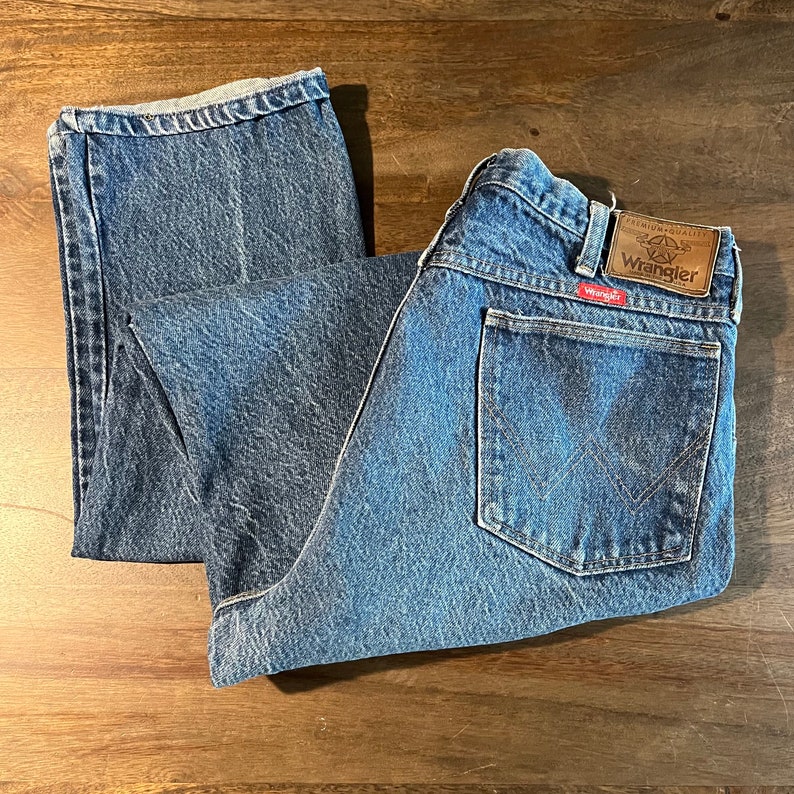 May include: A pair of blue denim jeans with a brown leather patch that says "Premium Quality Wrangler" and a red patch that says "Wrangler".