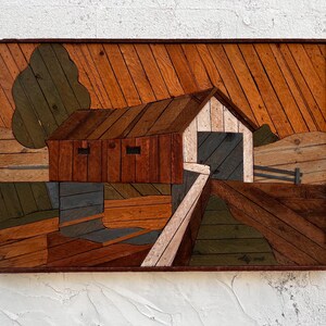 May include: Wooden art piece depicting a rustic covered bridge scene. The artwork features a bridge, a tree, and a fence, all crafted from various shades of wood. The piece is framed in a dark brown border.