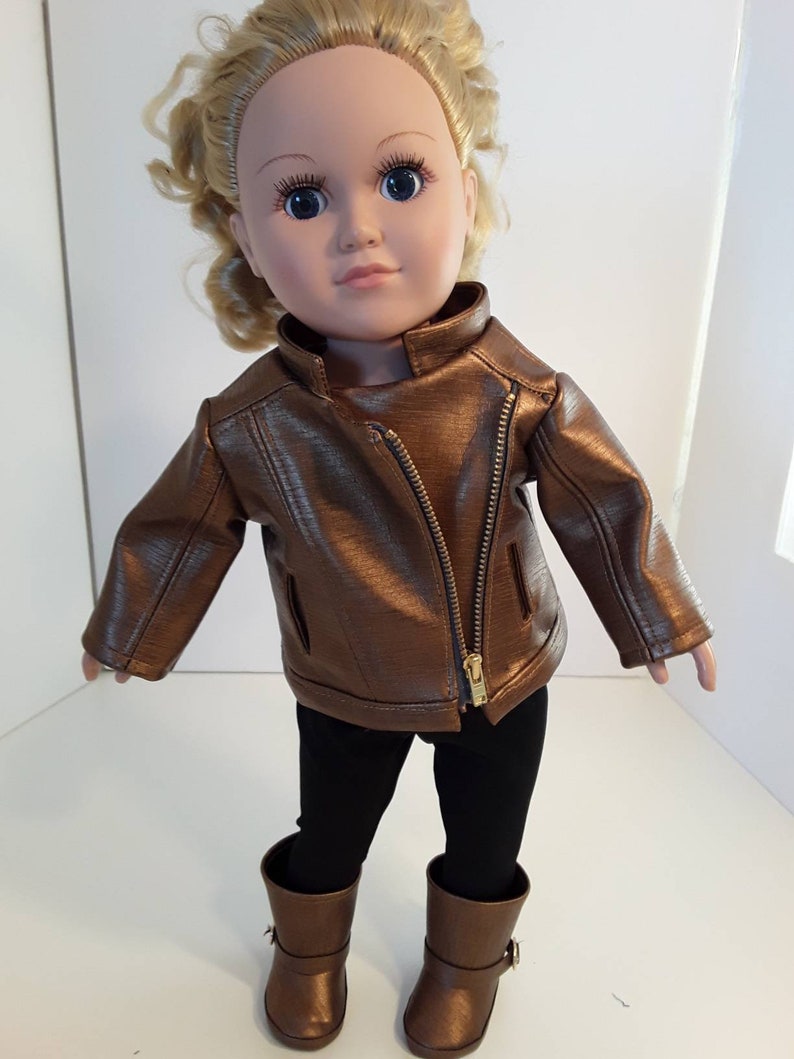 May include: A doll wearing a brown leather jacket, black leggings, and brown boots.