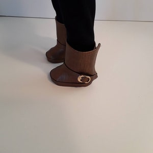 May include: A pair of brown leather boots with a gold buckle. The boots have a slightly pointed toe and a low heel.