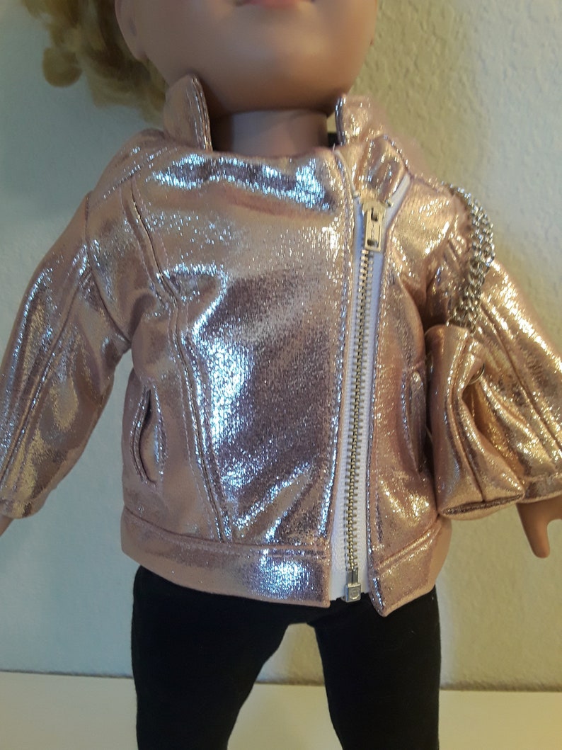 May include: A rose gold metallic jacket with a zip closure. The jacket has a shiny finish and is designed for a doll.