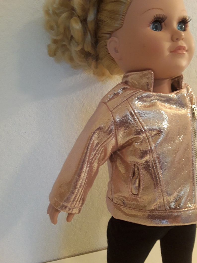 May include: A doll wearing a rose gold faux leather jacket with a zip closure. The jacket has a shiny finish and a pocket on the left side.