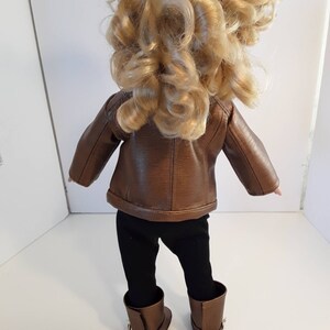 May include: A brown leather jacket with a zipper closure, black leggings, and brown boots. The doll is wearing the outfit.