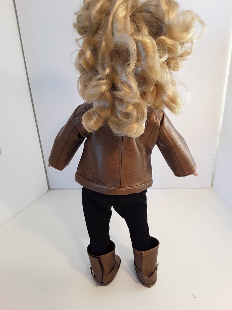 May include: A brown leather jacket with a zipper closure, black leggings, and brown boots. The doll is wearing the outfit.