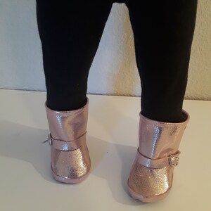 May include: A pair of pink glitter boots with a buckle on each boot.
