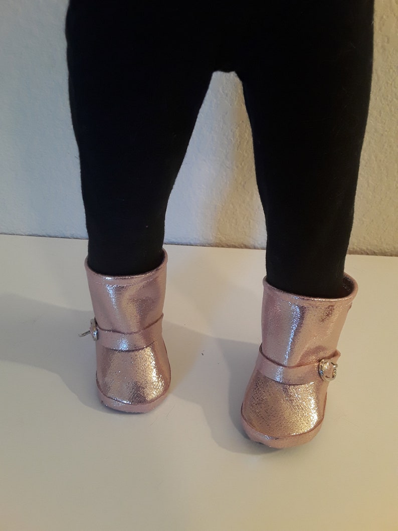 May include: A pair of pink glitter boots with a buckle on each boot.