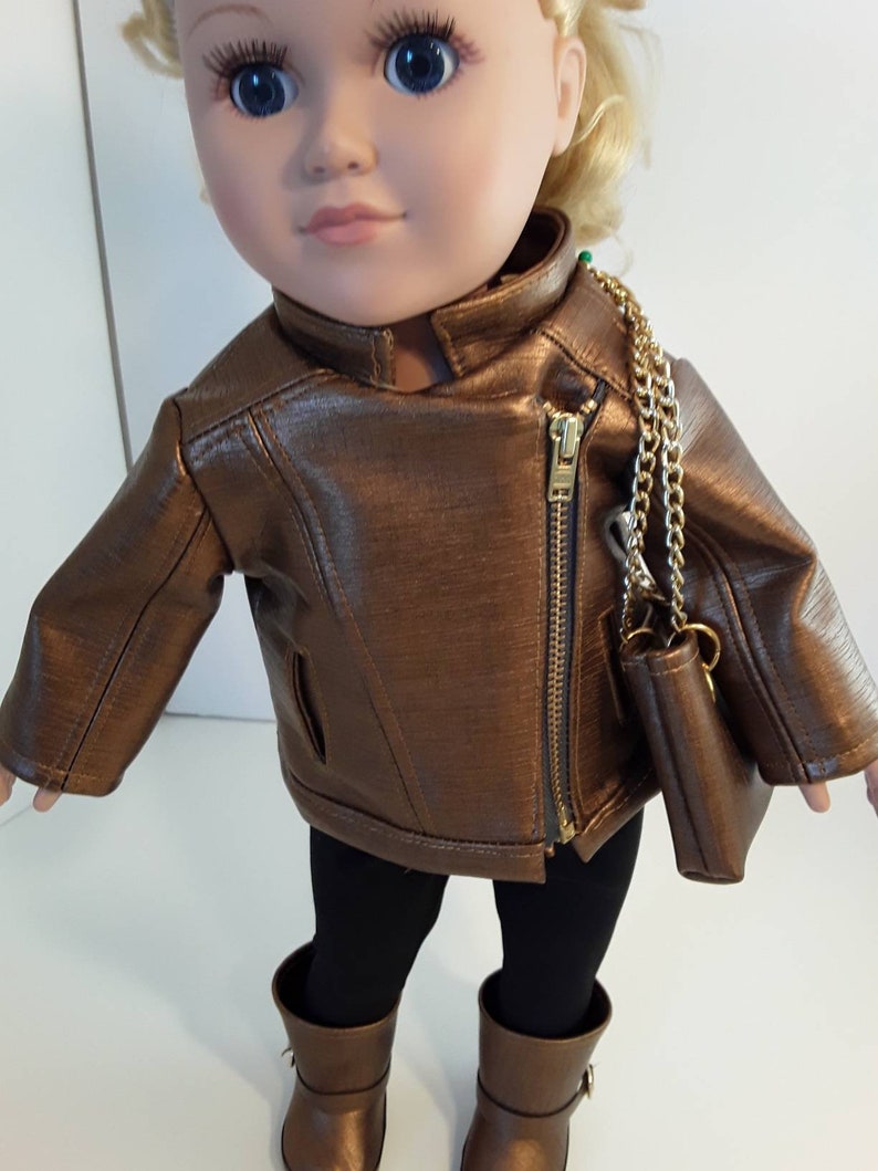 May include: A brown leather jacket with a gold zipper and a gold chain strap purse. The jacket is worn by a doll with blonde hair and blue eyes.