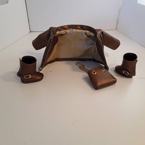 May include: A brown leather jacket with a zipper closure, a small brown leather purse with a gold chain strap, and two brown leather boots.