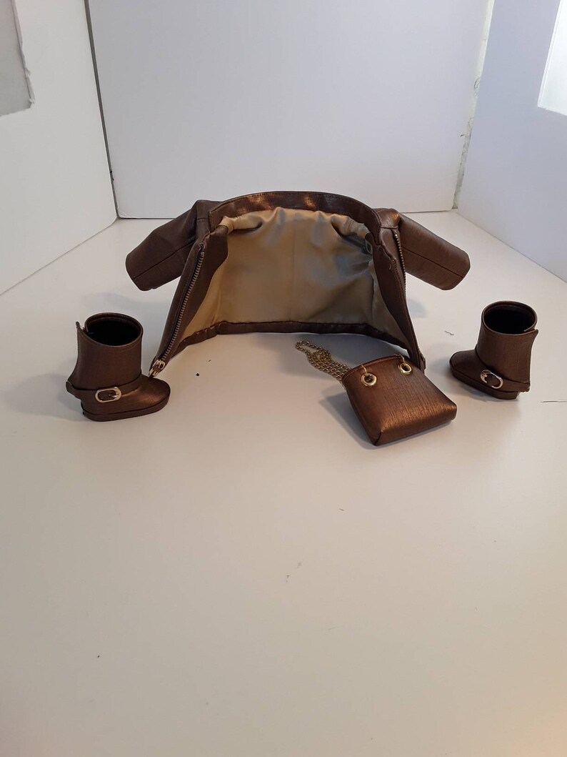 May include: A brown leather jacket with a zipper closure, a small brown leather purse with a gold chain strap, and two brown leather boots.