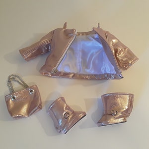 May include: A rose gold doll outfit set including a jacket, boots, and a small purse with a chain strap.