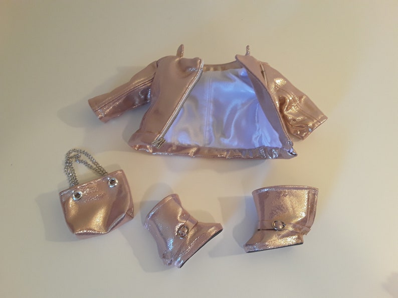 May include: A rose gold doll outfit set including a jacket, boots, and a small purse with a chain strap.