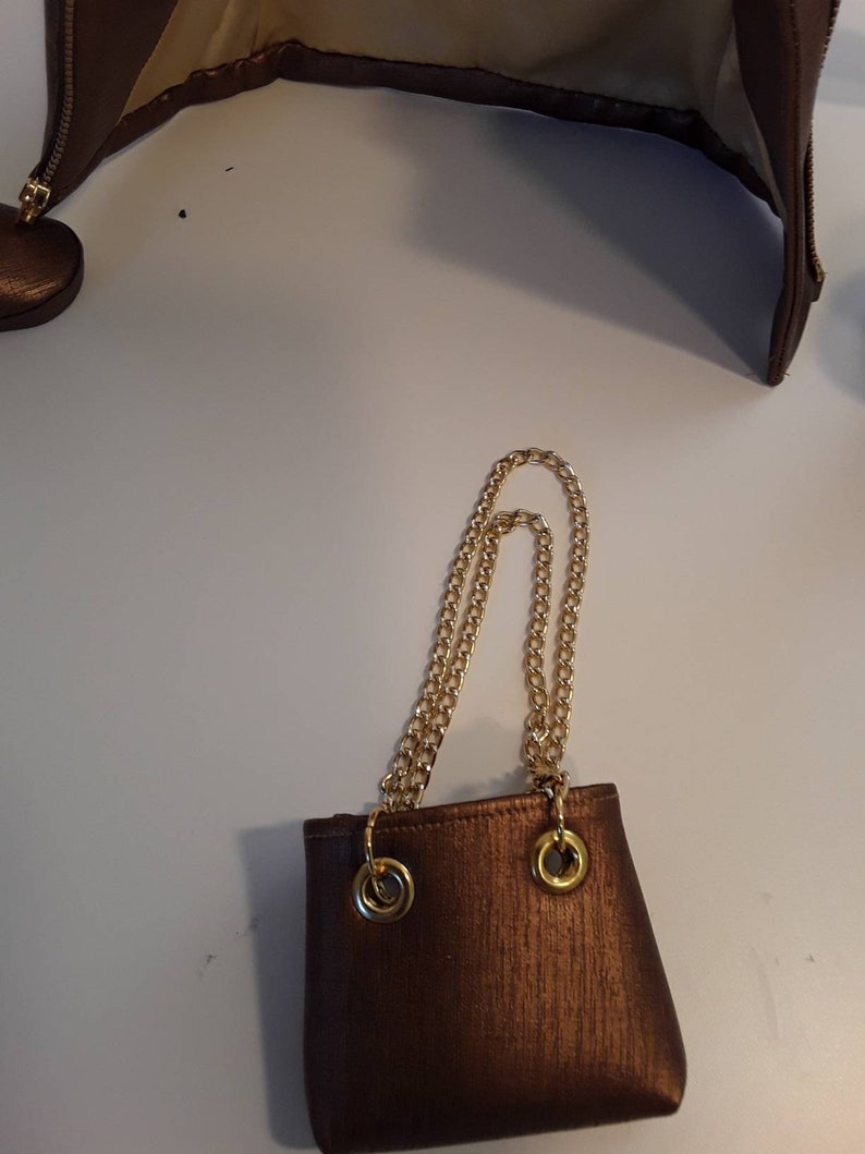 May include: A small brown purse with a gold chain strap. The purse has a textured fabric and two gold rings on the top.