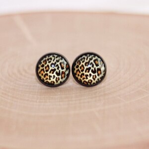 May include: A pair of oval-shaped stud earrings with a black metal setting and a leopard print design.