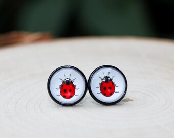 May include: A pair of ladybug earrings with red and black details. The earrings are made of glass and have a round shape.