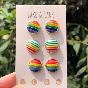 May include: A set of six rainbow-colored stud earrings. The earrings are arranged in pairs on a white card with the text "LAKE & LARK" printed at the top. The card also includes social media icons and the website address "www.lakeandlark.com".