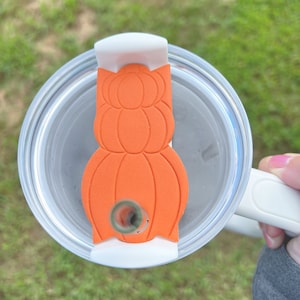 May include: A white and orange pumpkin-shaped lid for a tumbler. The lid has a hole for a straw.