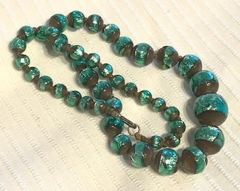 May include: A green and brown beaded necklace with a metallic sheen. The beads are round and have a striped pattern.