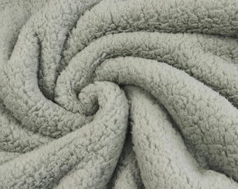 May include: A light gray fabric with a thick, plush, and curly sherpa texture. The material is arranged in soft, swirling folds that highlight the dense, fuzzy pile and the consistent neutral color throughout the entire surface of the textile.
