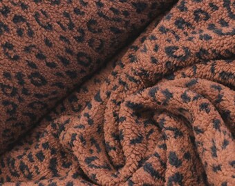 May include: A textured fabric featuring a repeating leopard print pattern in shades of dark brown and black. The material has a thick, fuzzy, and plush surface with deep folds and creases that highlight the soft, dense pile of the textile.