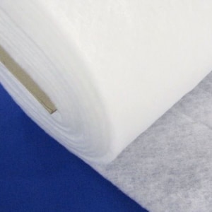 Può includere: Un rotolo di tessuto di interfodera bianco, un tipo di materiale fusibile utilizzato in progetti di cucito e quilting. Il tessuto è arrotolato e parzialmente srotolato, rivelando il colore bianco e la trama.