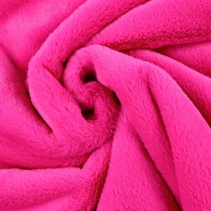 Può includere: Primo piano di un tessuto morbido e rosa con una texture pelosa. Il tessuto è piegato e drappeggiato, creando un motivo a spirale.
