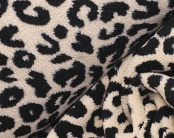 May include: A plush, textured fabric featuring a high-contrast leopard print pattern. The material displays a repeating design of irregular black spots set against a creamy off-white background, with a soft, fuzzy surface texture throughout.