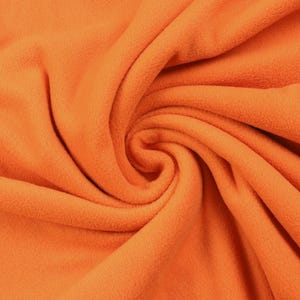 Può includere: Primo piano di un vibrante tessuto in pile arancione, disposto a spirale. Il materiale morbido e strutturato è illuminato in modo uniforme, mettendo in risalto la sua superficie soffice e il colore caldo. Le pieghe e le curve del tessuto aggiungono profondità.