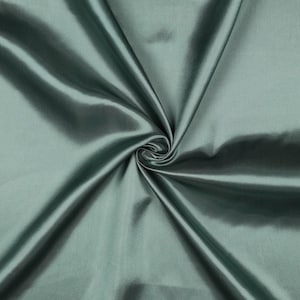 Può includere: Primo piano di un tessuto color verde acqua con una lucentezza serica. Il tessuto è raccolto a spirale, creando pieghe e ombre che evidenziano la sua consistenza e le variazioni di colore. Il materiale appare liscio e lussuoso.