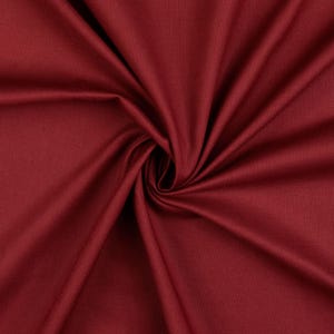 Puede incluir: Primer plano de una tela rojo intenso con un ligero brillo. El material está dispuesto en espiral, creando pliegues y sombras que resaltan su textura. El color es un tono rico y saturado, lo que sugiere un textil lujoso.