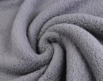 May include: A soft, grey fabric with a dense, curly, and textured pile surface. The material is arranged in a swirling, folded pattern that highlights the thick, plush, and fuzzy consistency of the textile, creating deep shadows and light highlights.