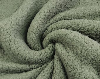 May include: A sage green fabric with a thick, plush, and curly sherpa fleece texture. The material is gathered into soft, swirling folds that highlight the dense, fuzzy pile and the consistent muted green color throughout the entire surface.