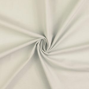 Op de afbeelding: Een close-up van een lichtgrijze stof met een gladde textuur. De stof is in een cirkelvormig patroon gerangschikt, waardoor een gevoel van beweging en diepte ontstaat. Het materiaal lijkt zacht en soepel, geschikt voor kleding of interieurdecoratie.