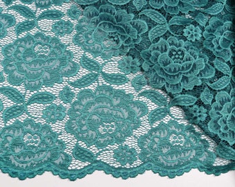 Pode incluir: Close-up de tecido de renda verde-azulado com um padrão floral. A renda apresenta grandes e detalhados desenhos florais e pequenos detalhes florais. O tecido está dobrado, mostrando o intrincado trabalho aberto e a textura da renda.