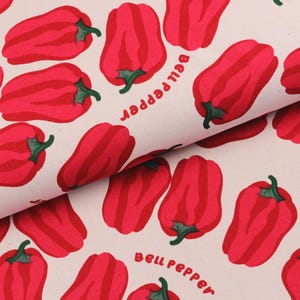 Op de afbeelding: Crèmekleurige stof met een herhaald patroon van rode paprika's met groene stelen. De woorden "bell pepper" zijn in een gebogen lettertype gedrukt. De paprika's hebben rode strepen.