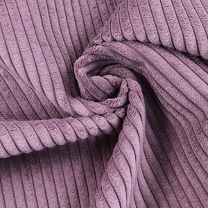 Könnte beinhalten: Nahaufnahme eines weichen, violetten Cordstoffs mit gerippter Textur. Der Stoff ist gefaltet und drapiert, wodurch die Textur und der Fall des Materials sichtbar werden.