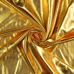 May include: A close-up of a gold fabric with a shiny, metallic finish. The fabric is draped and folded, creating a swirling pattern.