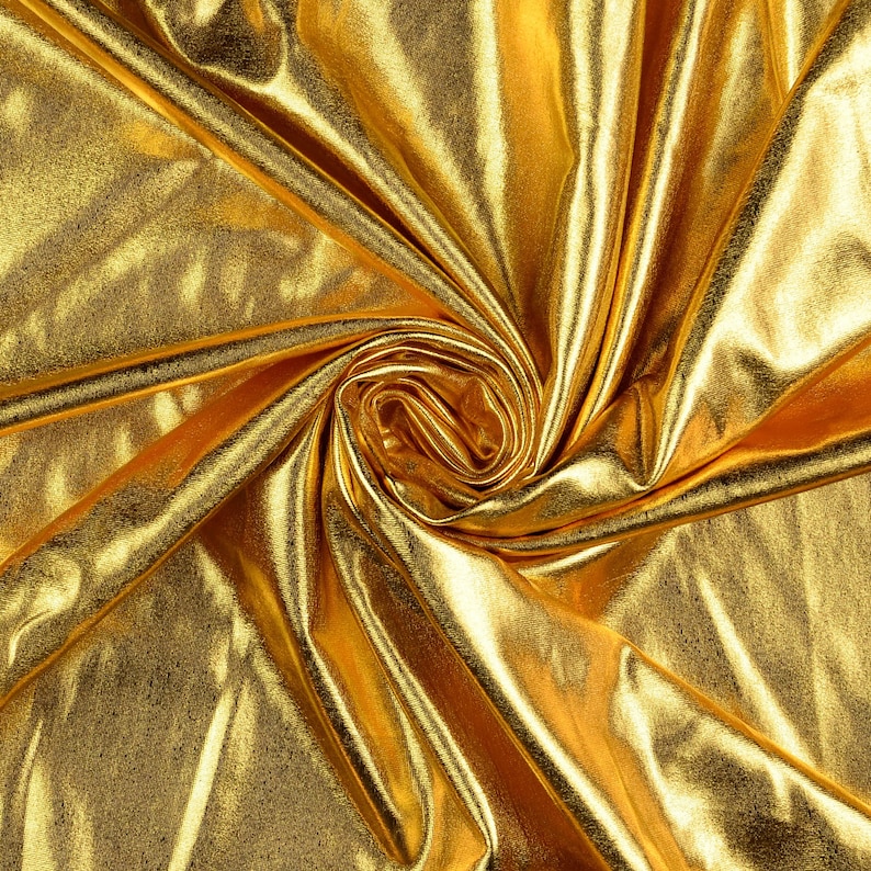 May include: A close-up of a gold fabric with a shiny, metallic finish. The fabric is draped and folded, creating a swirling pattern.