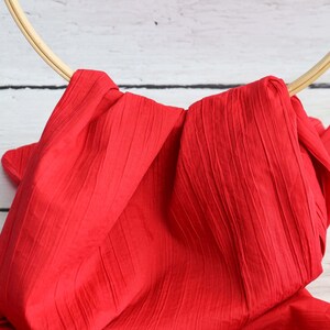 May include: Red fabric with a crinkled texture draped over a wooden hoop.