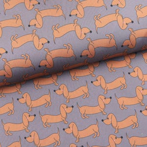Può includere: Un tessuto fantasia con illustrazioni di cani bassotto arancioni su sfondo grigio. I cani sono raffigurati in varie pose con contorni neri. Il tessuto ha un aspetto strutturato.