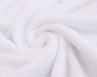 May include: A solid white blanket featuring a soft, plush, and fuzzy texture. The fabric is arranged in a circular, swirling pattern that creates deep folds and shadows, highlighting the dense, fleecy material of the textile throughout.