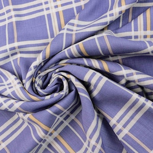 Puede incluir: Tela morada con un patrón de cuadros blancos y amarillos. La tela está doblada y drapeada, mostrando la textura y el tejido.