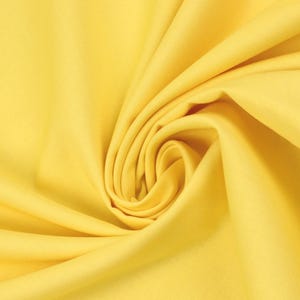Op de afbeelding: Close-up van een heldergele stof met zachte plooien en een wervelend patroon. De stof heeft een gladde textuur en de kleur is consistent. De stof wordt waarschijnlijk gebruikt voor kleding of interieurdecoratie.